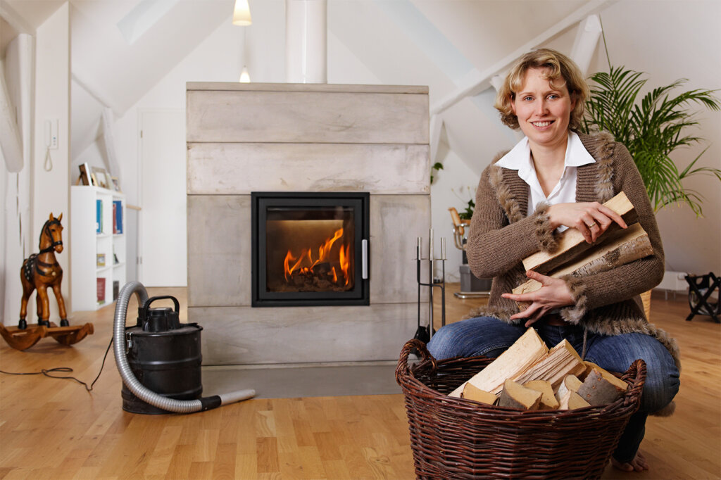 Femme avec du bois sur les bras devant la cheminée et l'aspirateur à cendres