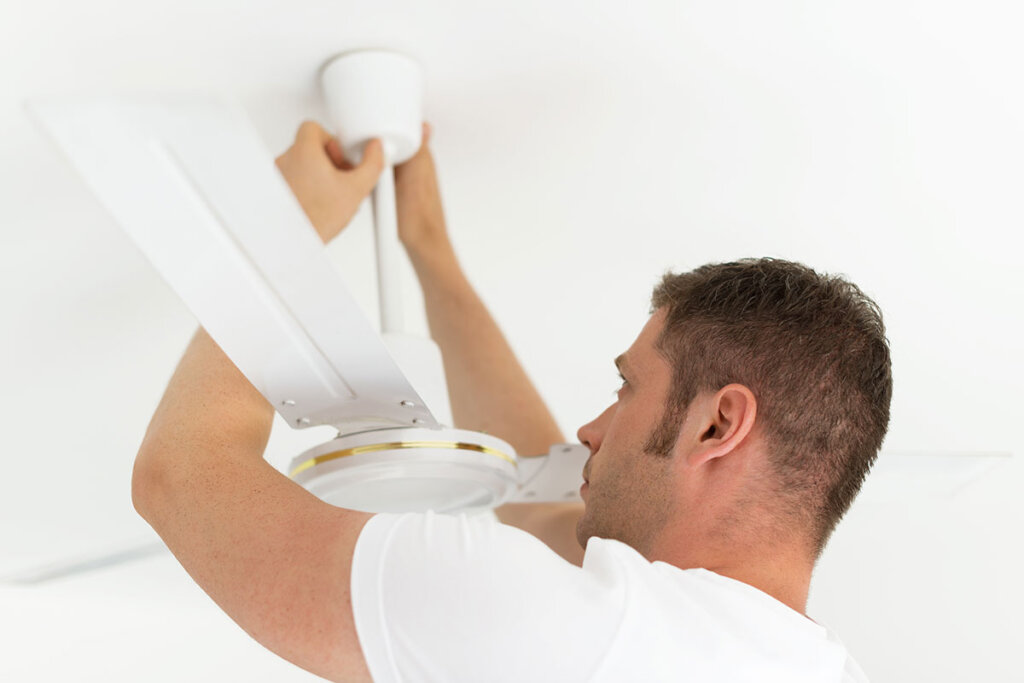 Un homme installe un ventilateur de plafond