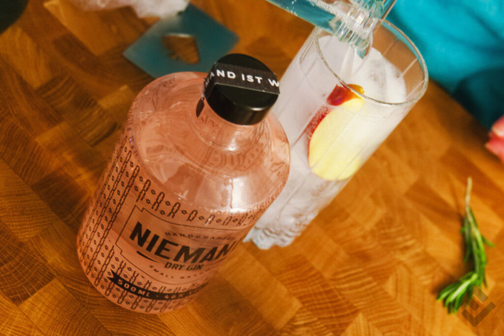 Bottle of Niemand Gin and a glass with garnishes on a wooden table.