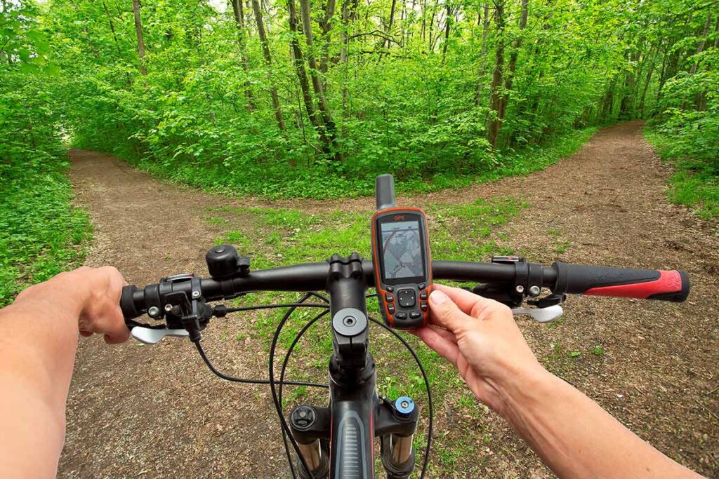 un cycliste regarde son navi avant de traverser un chemin dans la forêt