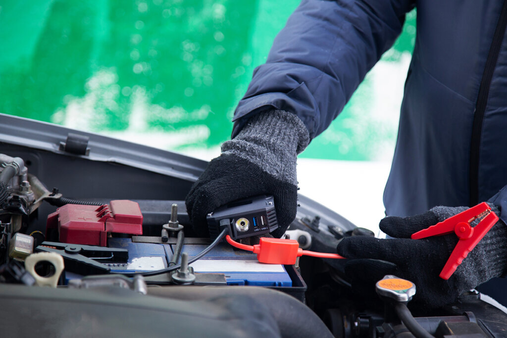 L'homme connecte le booster à la batterie de la voiture