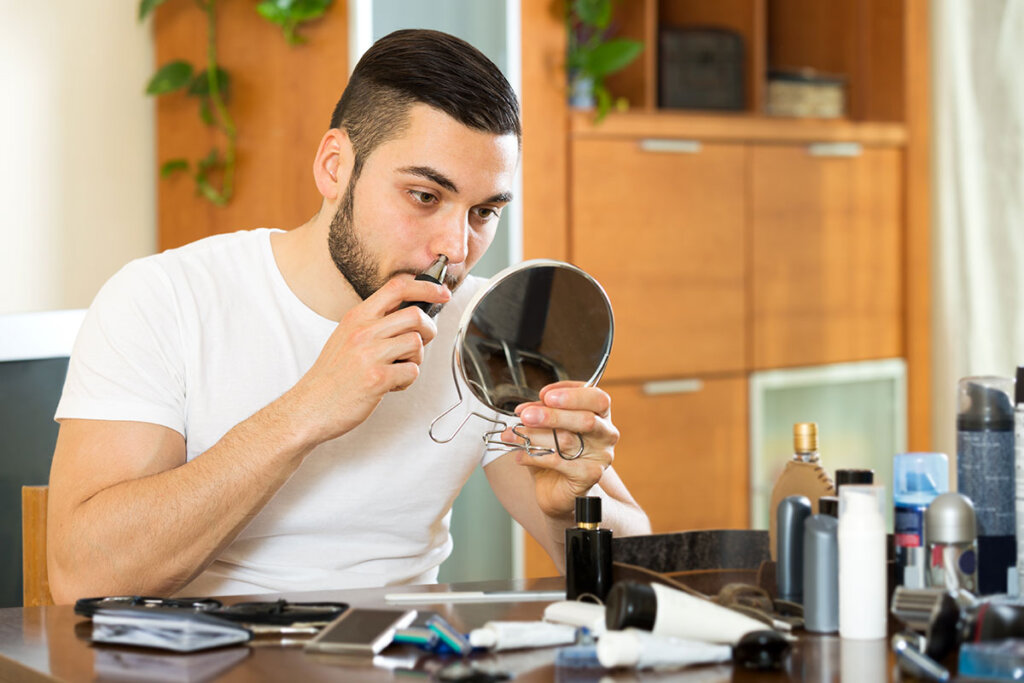 Homme trimant des poils de nez devant un petit miroir