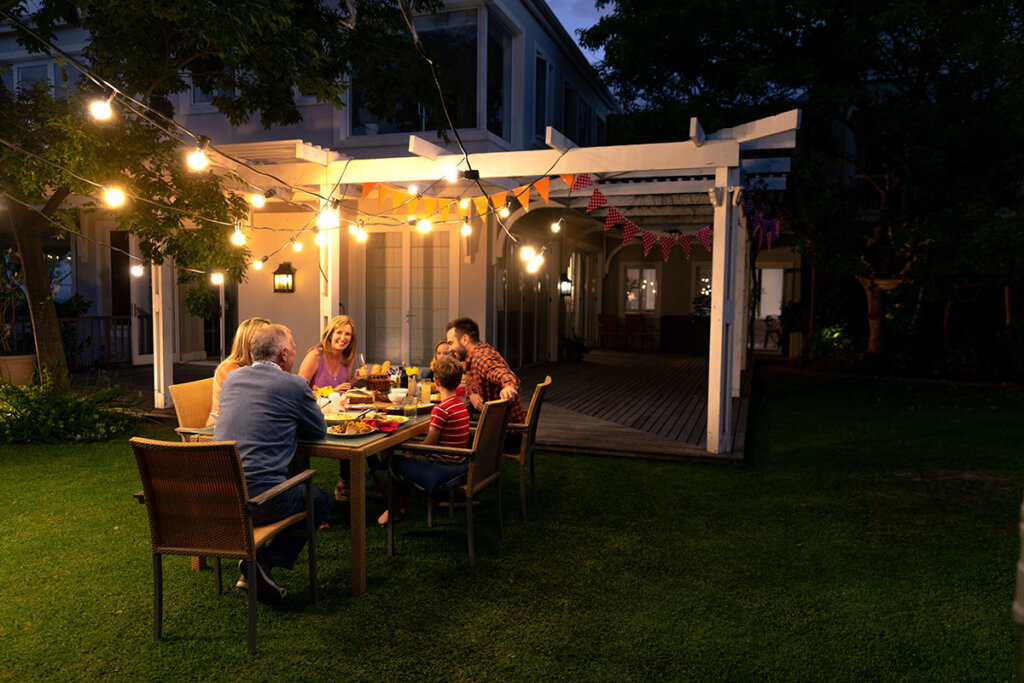 la famille mange ensemble dans le jardin avec une chaîne lumineuse