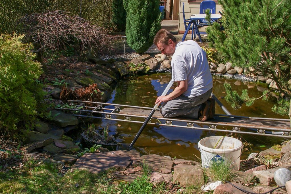 Un homme nettoie un étang de jardin avec un aspirateur de boue d'étang