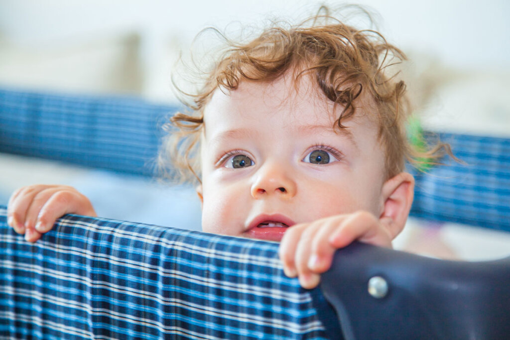 Bébé dans le lit de voyage regarde par-dessus le bord