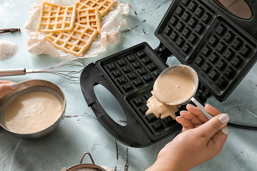 Femme verse la pâte à gaufre dans le gaufrier