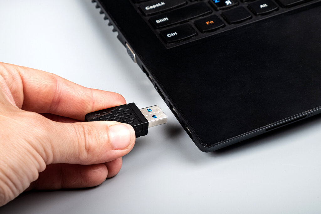 La personne insère la clé WLAN dans le slot USB de l'ordinateur portable.